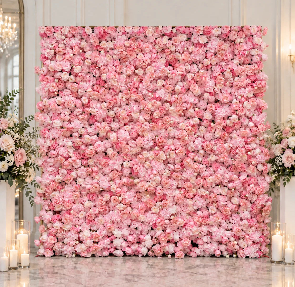 A large square floral wall backdrop covered in dense pink and white flowers, set in an elegant indoor venue with marble flooring, candles, and floral arrangements on both sides.